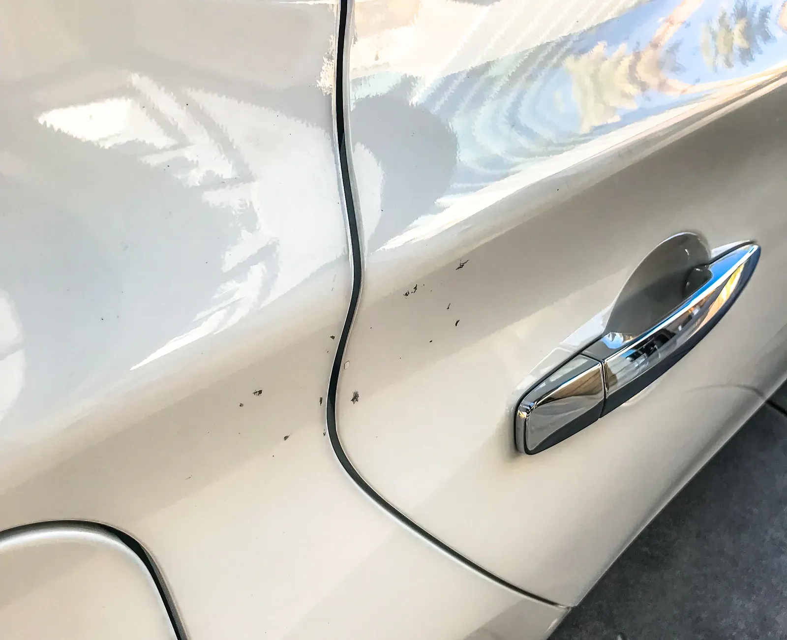 Small dings and paint marks on a white car door near the handle