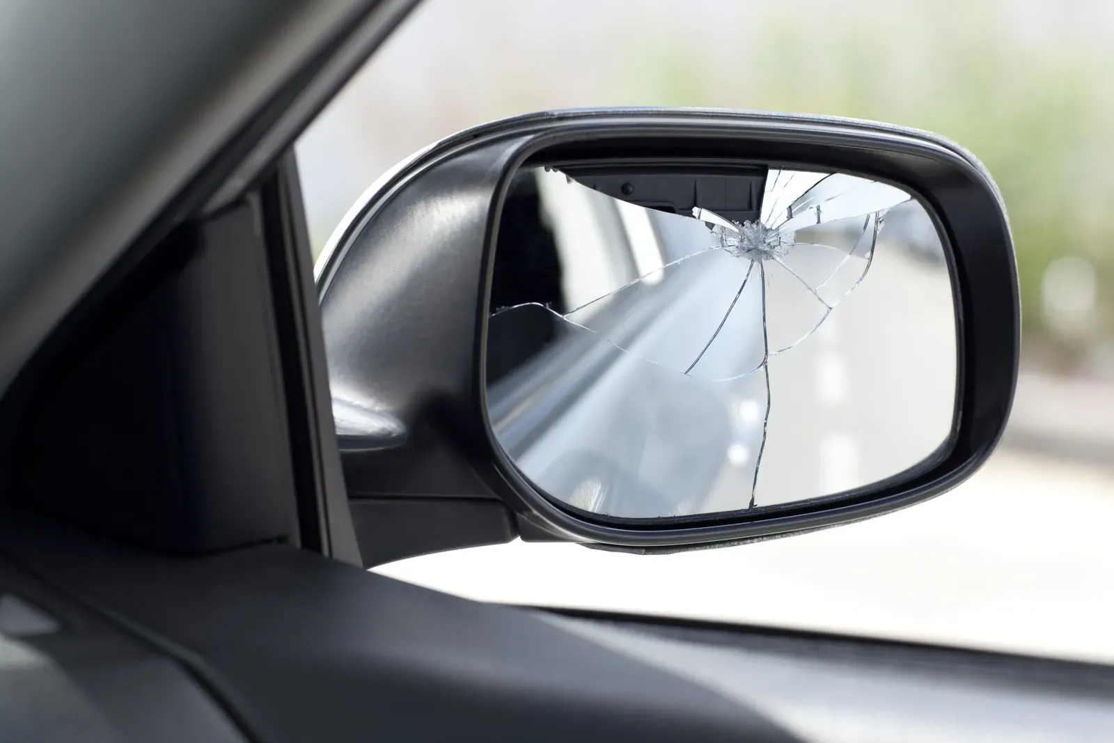 Broken side mirror with shattered glass hanging from a car door