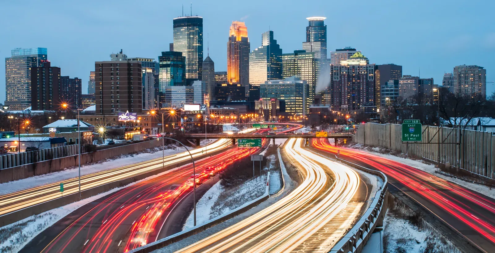 Minneapolis skyline at dusk over a snow-lined interstate during the winter commute